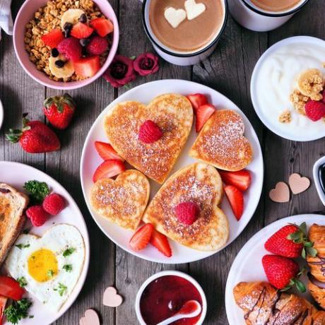 sõbrapäeva või emadepäeva hommikusöögilauastseen tumedal puidust taustal südamekujuliste pannkookide, munade ja armastuse teemalise toiduga