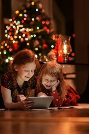 õed, kes kasutavad jõulude ajal põrandal tahvelarvutit